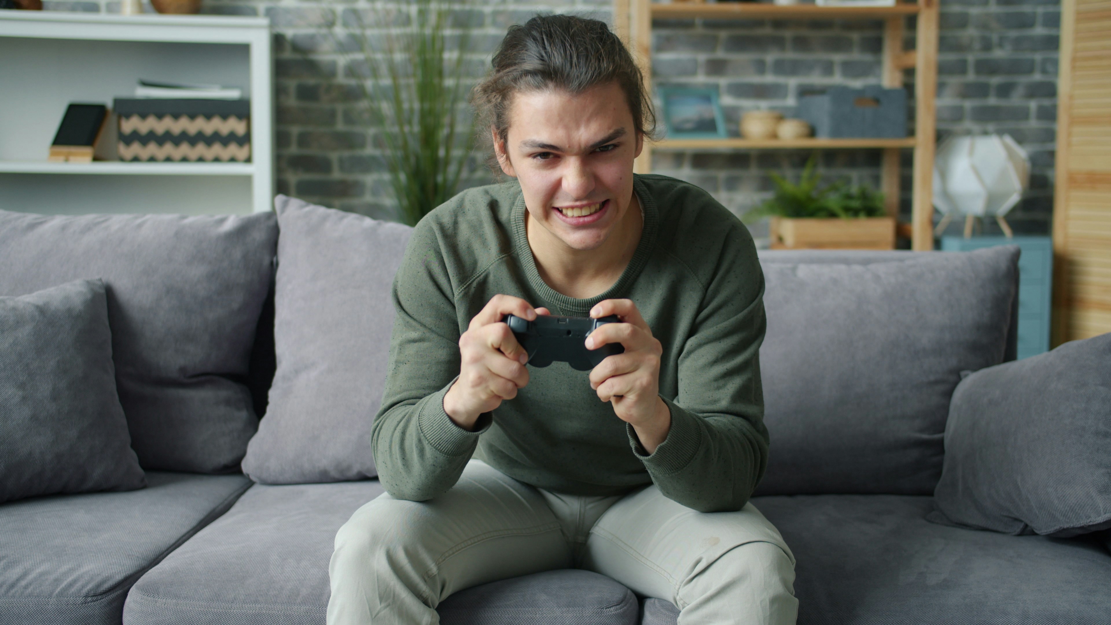Emotional young man playing video game at home sitting on sofa at home spending leisure time in modern apartment. Youth, lifestyle and fun concept.